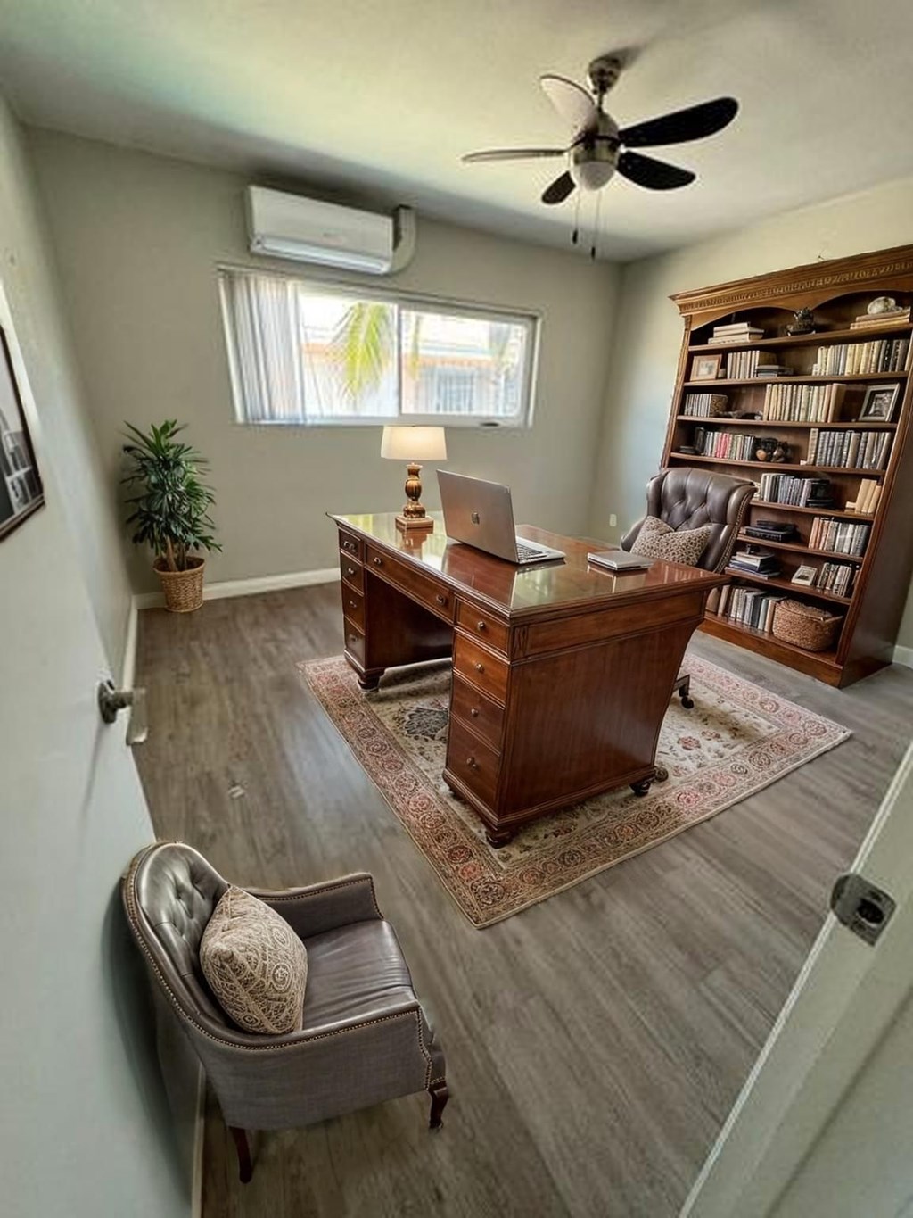 A room with a ceiling fan, a desk with a laptop, a chair, and a bookshelf.