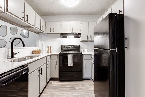 A black refrigerator stands in a kitchen with white cabinets and a black stove.