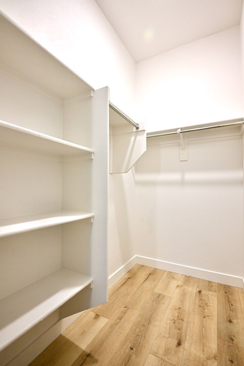 A white closet with shelves and a wooden floor.