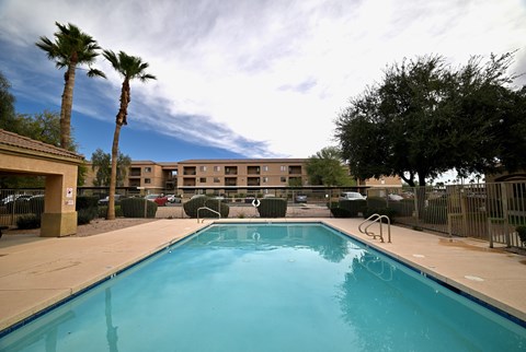 A swimming pool surrounded by palm trees and a building in the background.