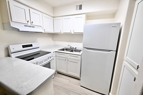 A white kitchen with a refrigerator, sink, and oven.