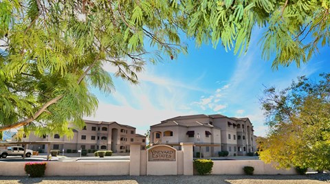A building with the sign "Vineyard Estates" is surrounded by trees and has a clear blue sky above.