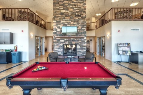 A pool table is in the middle of a room with a stone wall and a TV.