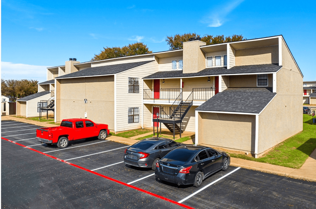 A red pickup truck is parked in a parking lot in front of a two-story apartment building.