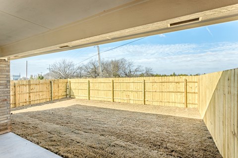 A backyard with a wooden fence and a carpeted ground.