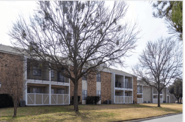 a picture of an apartment complex with trees in the foreground