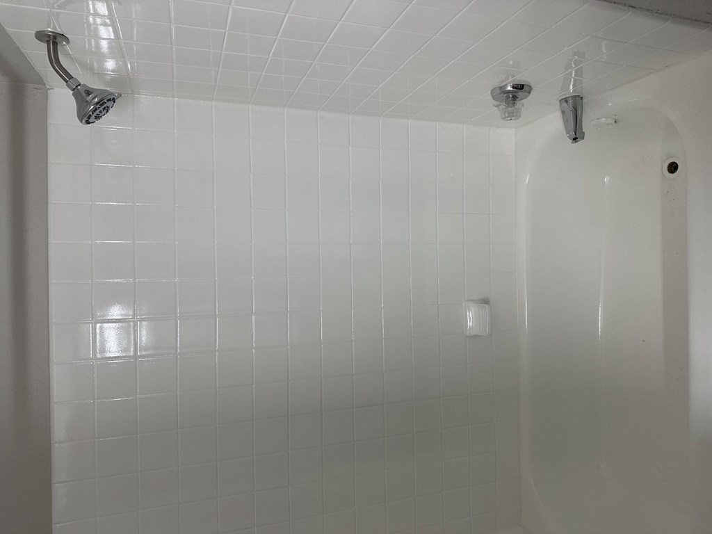 A white tiled shower area with a shower head and a hand held shower.