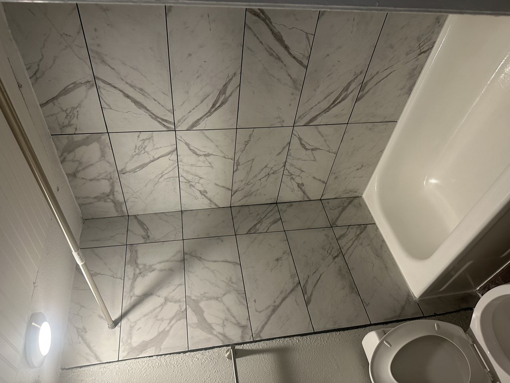 A white toilet is in a bathroom with marble tiles on the ceiling.