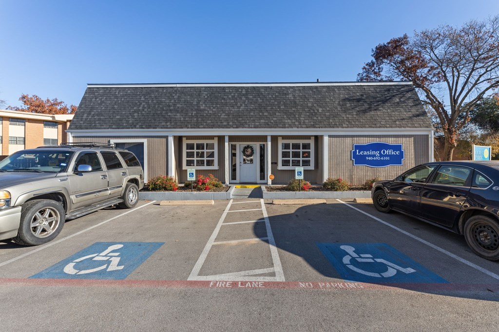 A parking lot in front of a Leasing Office with a black car and a silver truck.