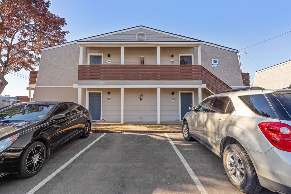 Two cars are parked in front of a two-story building with a garage.