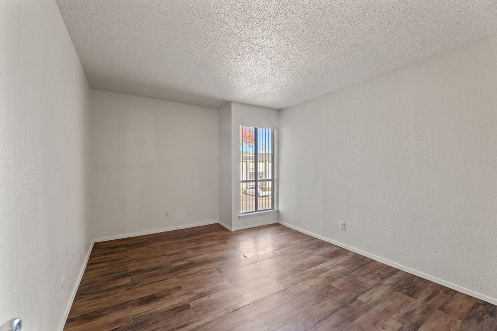 A room with wooden floors and a window with bars on it.