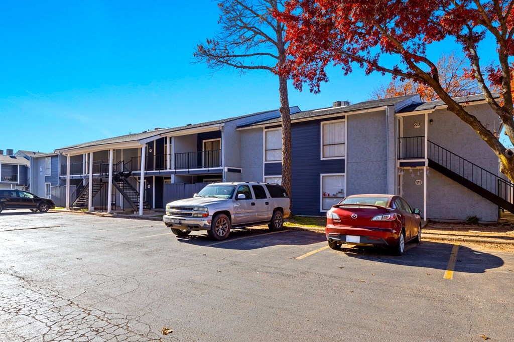 A red car is parked in a parking lot in front of a building.