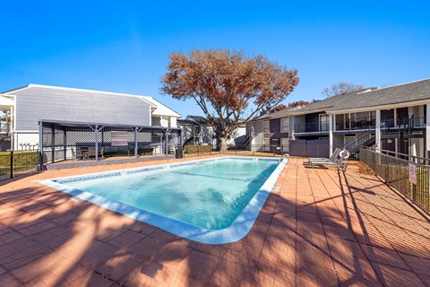 A small pool surrounded by a black fence and a tree with brown leaves.