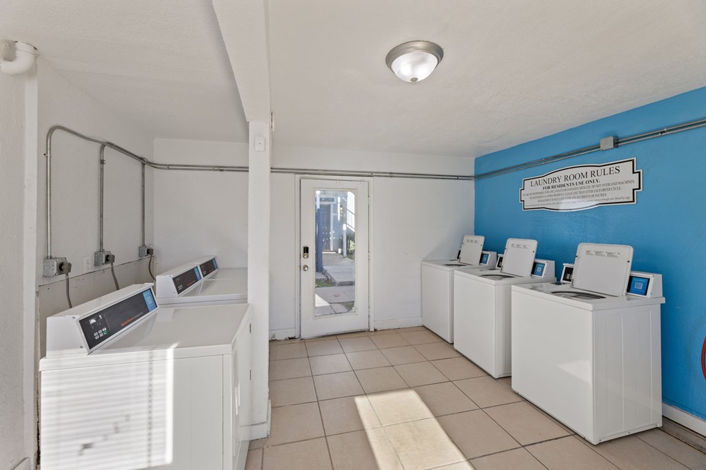 A laundromat with washers and dryers and a sign that says "Tailor Room Rules".