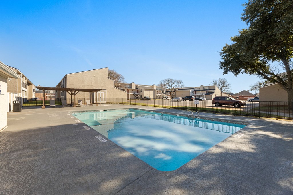 A swimming pool surrounded by a concrete patio and a fence.