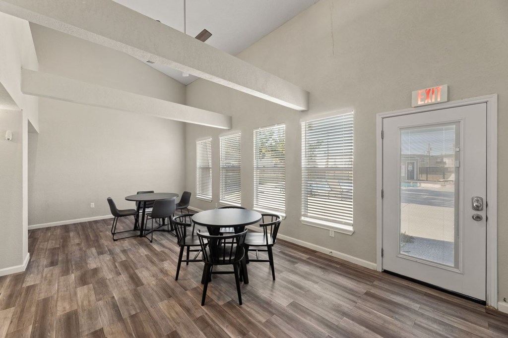 A room with a table and chairs and a door with an exit sign.