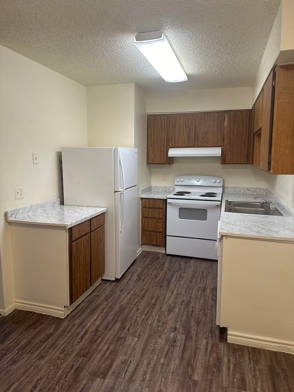 an empty kitchen with white appliances and wooden floors