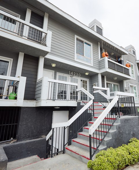 A grey building with a black railing and a red staircase.