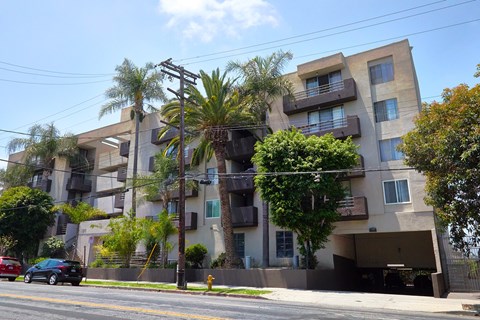 A black car is driving down a street past a building with balconies.