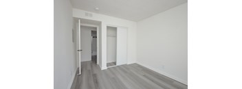 A room with white walls and wood flooring with a doorway leading to another room.