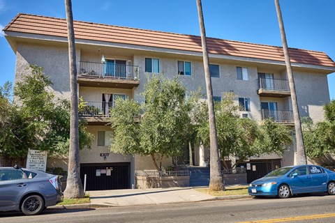 A blue car is parked in front of a building with a brown roof.