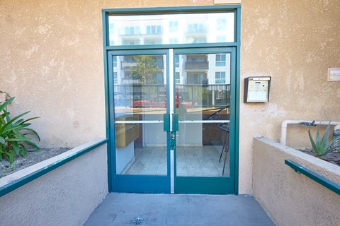 A green double door with a glass window and a metal handle.