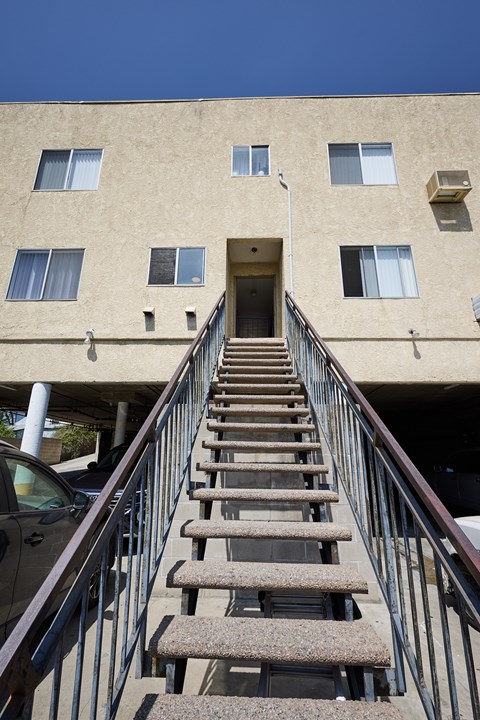 A staircase with a metal railing leads up to a doorway in a tan building.