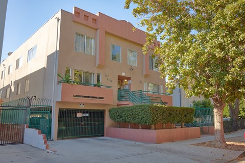 A modern two-story building with a green gate and a tree in front.
