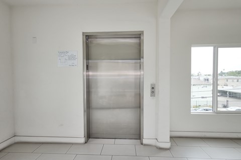 A stainless steel elevator in a white room with a paper on the wall.