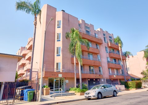 A silver car is parked in front of a pink building with palm trees.