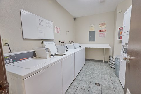 A laundromat with a white dryer and washer, a white ironing board, and a white sink.