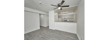 A room with a ceiling fan and a kitchenette in the corner.