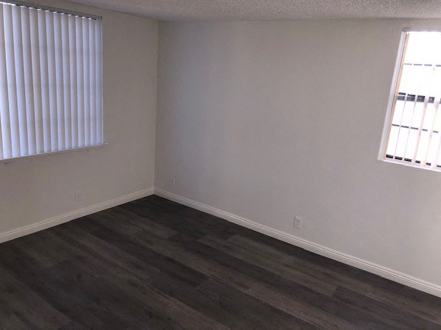 an empty room with wood flooring and two windows