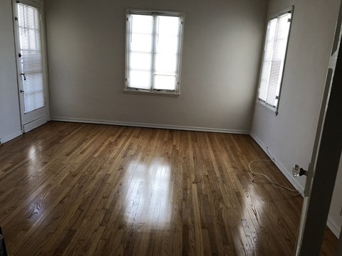 an empty room with wooden floors and two windows