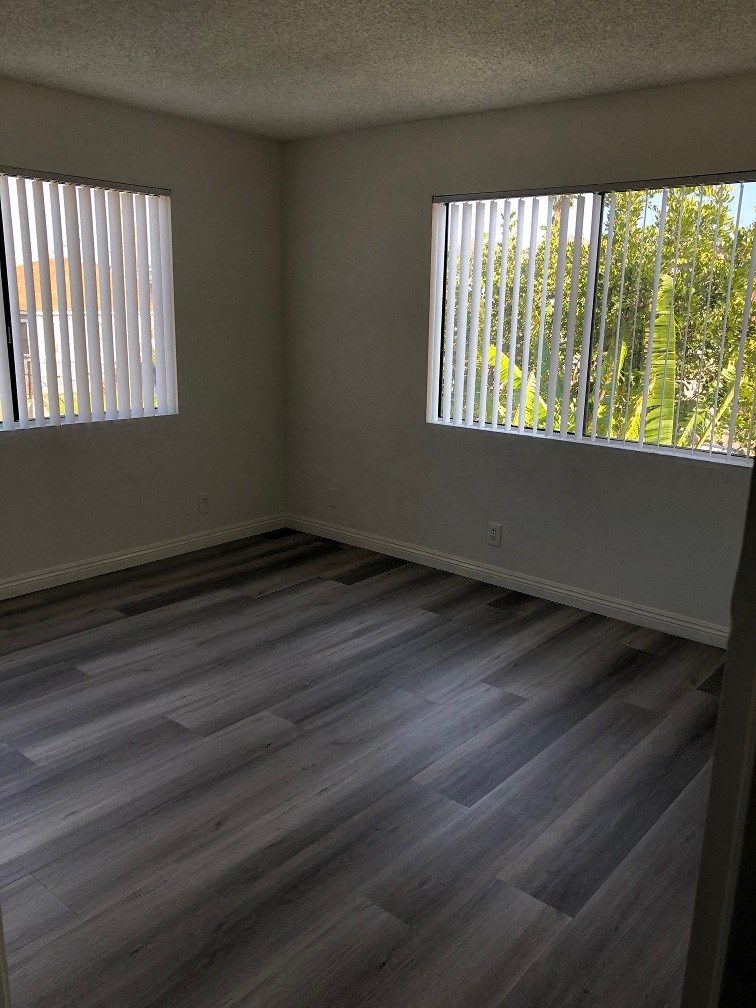 an empty room with wooden floors and two windows