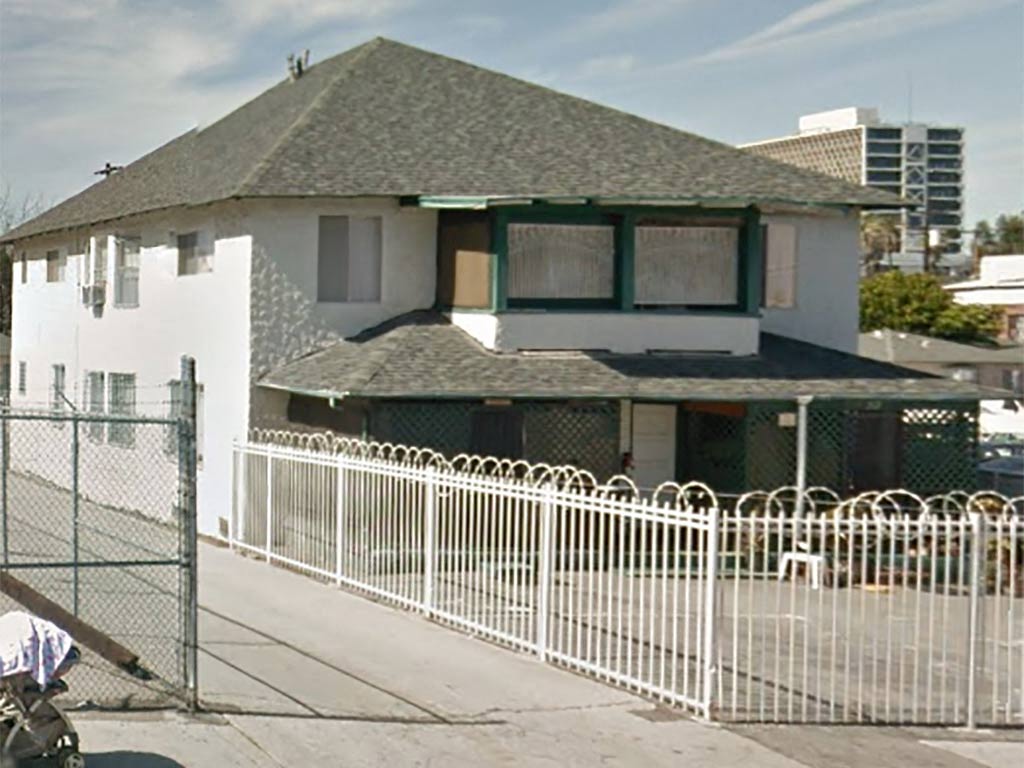 A white house with a green roof and a white fence in front.