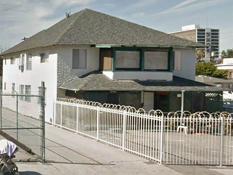 A white house with a green roof and a white fence in front.