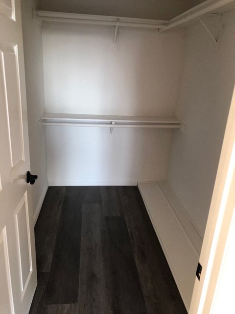 a room with wooden floors and a white wall with a bench