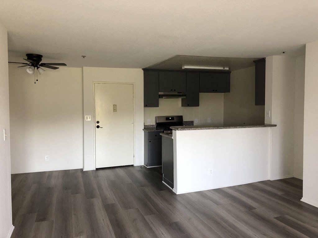an empty living room with a kitchen and a ceiling fan