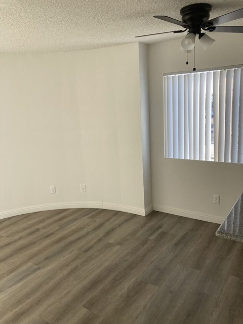 an empty living room with a window and a ceiling fan