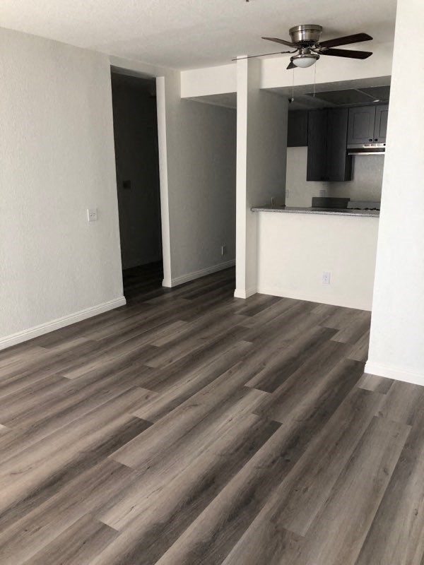 an empty living room with wooden floors and a kitchen