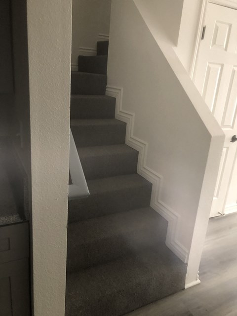 A staircase with a white railing and grey carpet.