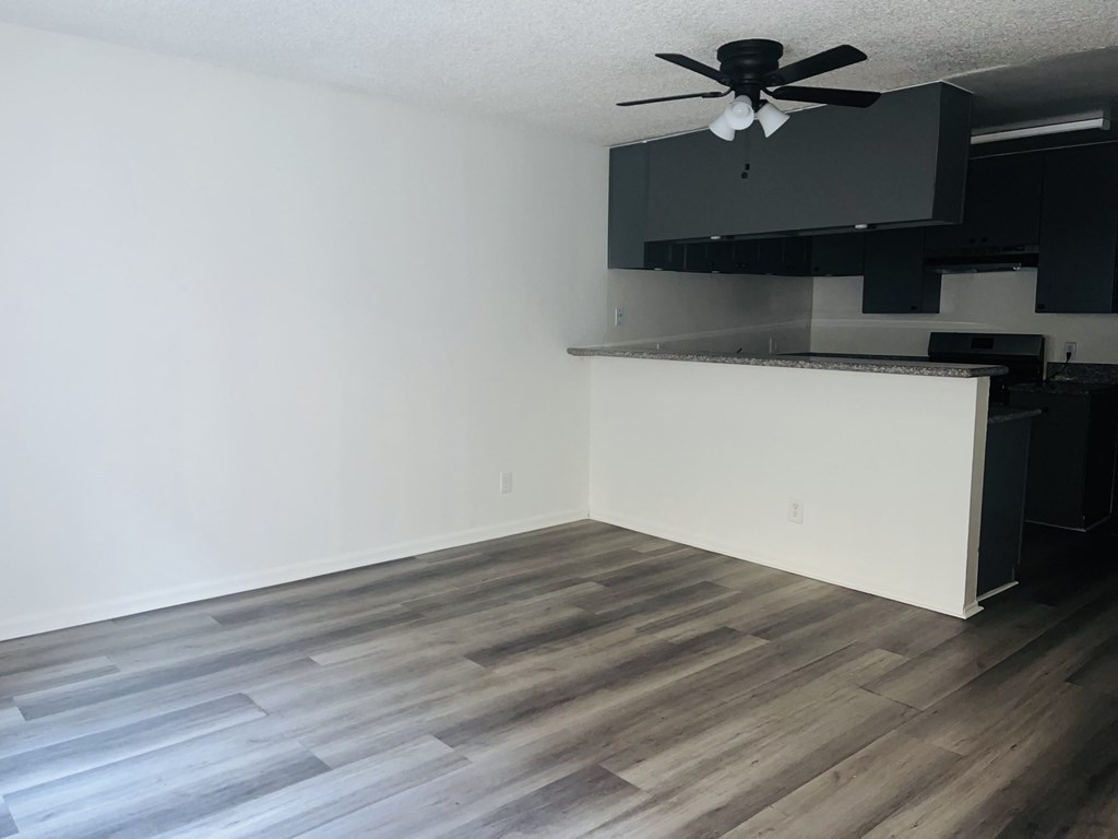 A room with a ceiling fan and a kitchen area with black cabinets.