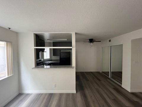 an empty living room with a kitchen and a ceiling fan