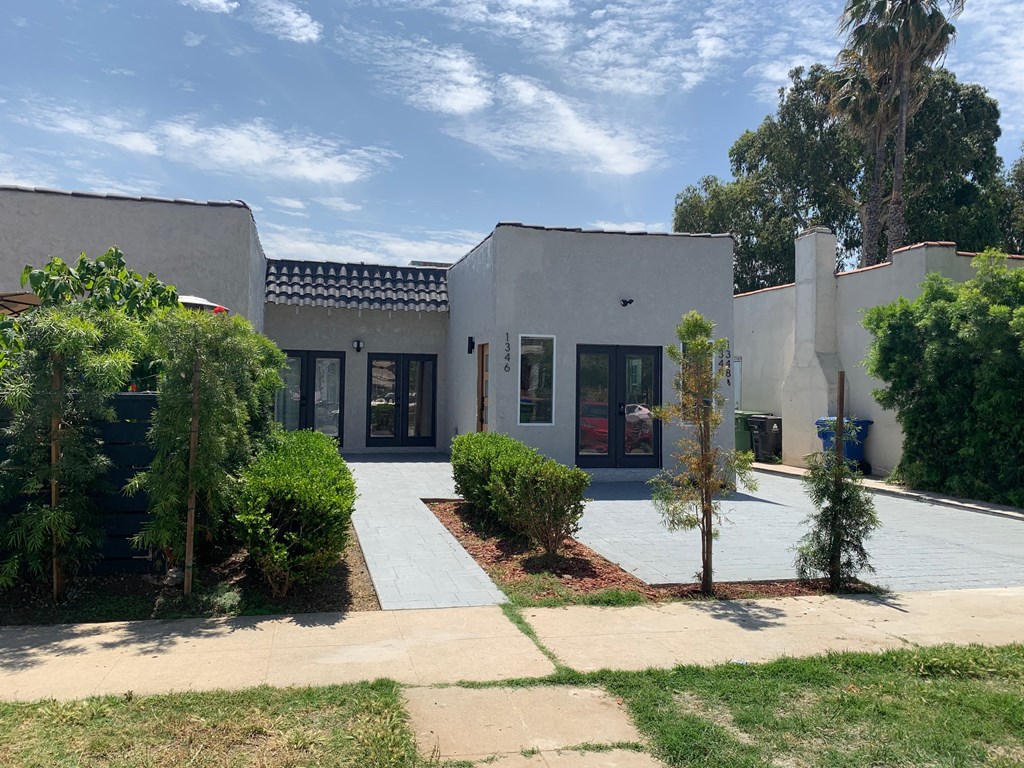 the exterior of a white house with trees and a sidewalk