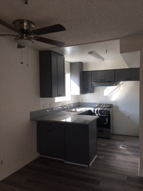 an empty kitchen with black cabinets and a ceiling fan