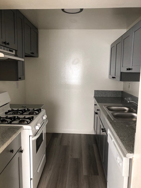an empty kitchen with white appliances and wood flooring