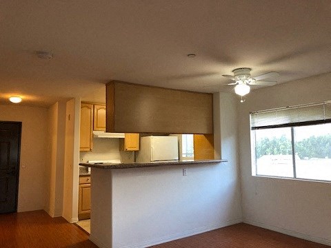 an empty living room with a kitchen and a ceiling fan