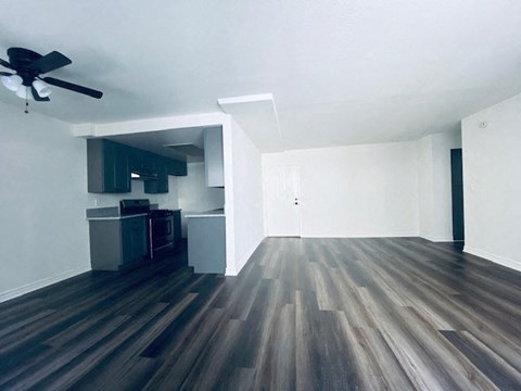 an empty living room with wood floors and a kitchen