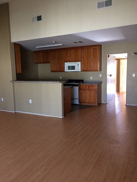 an empty kitchen with wooden floors and a microwave and cabinets